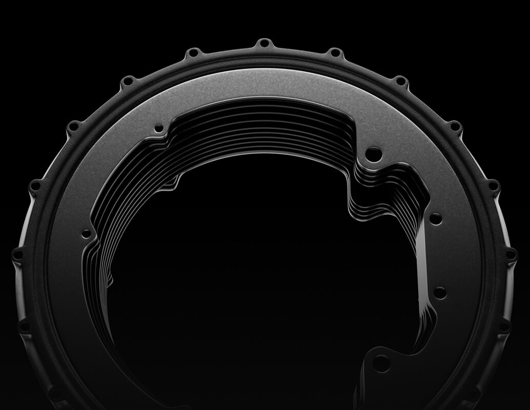 Close-up view of a circular metallic gear or mechanical component with a series of layered, curved ridges against a black background.