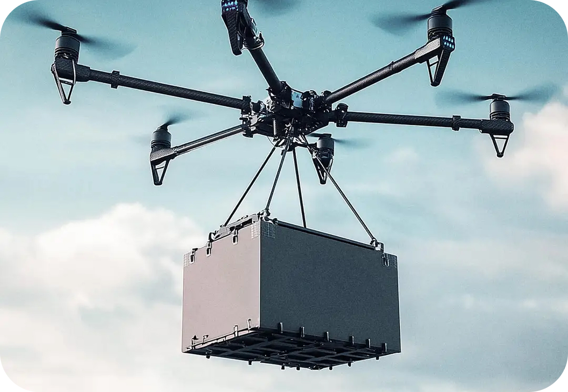 A large drone with multiple rotors is flying in the sky, carrying a rectangular gray delivery box suspended by cables.