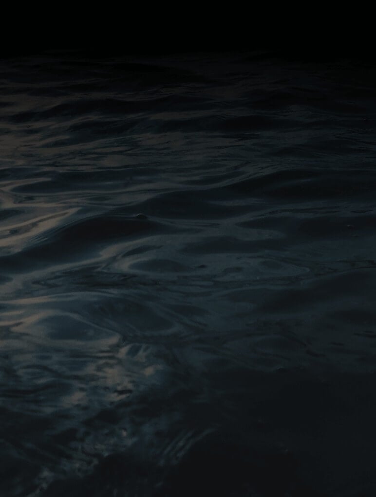 Dark, rippling water with subtle reflections under low light, creating a serene yet mysterious atmosphere.